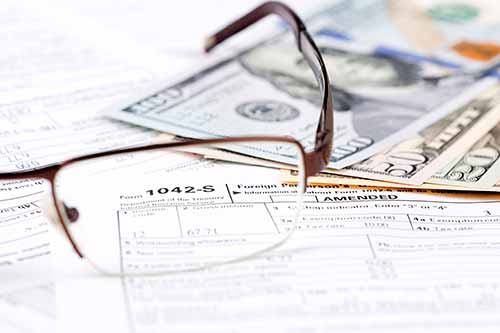 A Reading Glass and Cash on Top of Paper Applications and Bills.